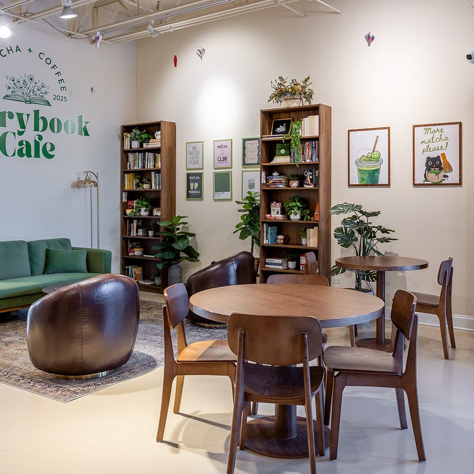 Storybook Cafe interior with green sofa, wooden tables, bookshelves, plants, and matcha-themed wall art.